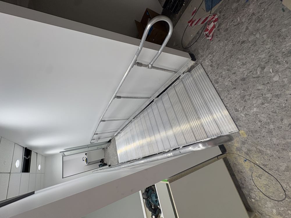 Modular aluminium access ramp with handrails to both sides, viewed from the bottom of the run, on a retail fitout in Rye.